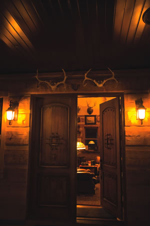 A warm, welcoming entrance with log siding, amber lighting and towering double doors sets the tone for