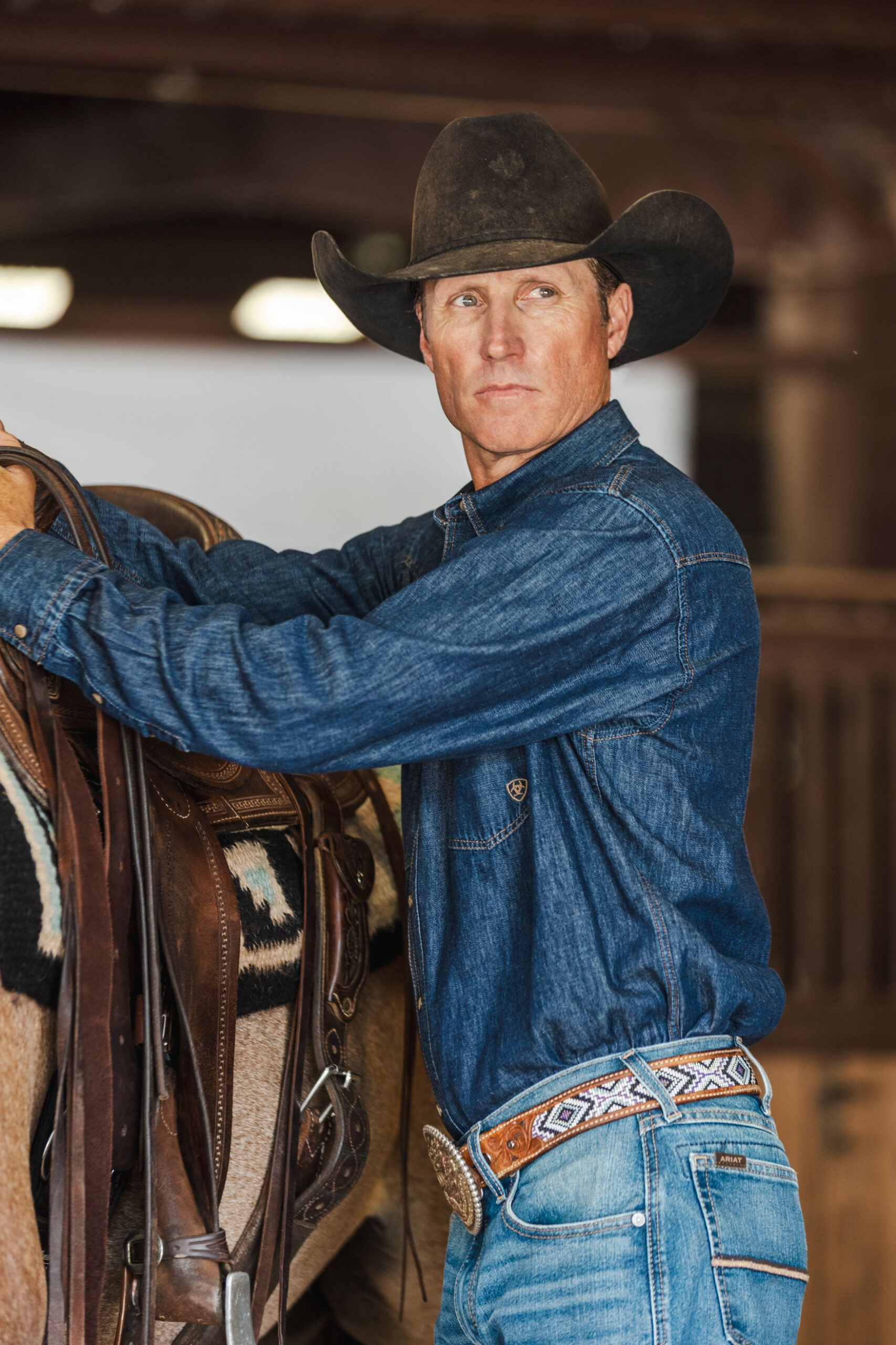 man in full denim & black felt saddling a horse