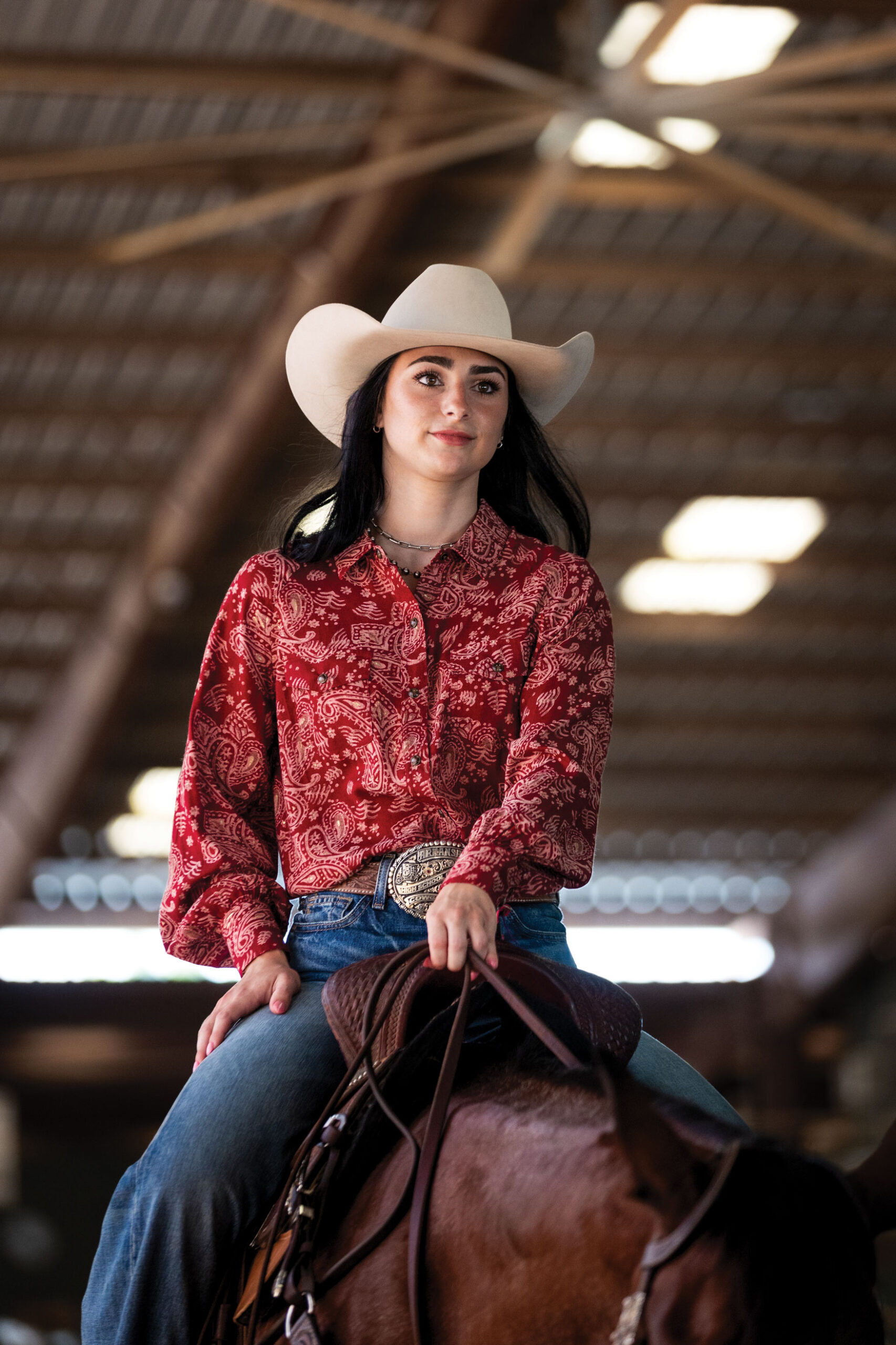 girl in bone colored fely, red button down on a horse