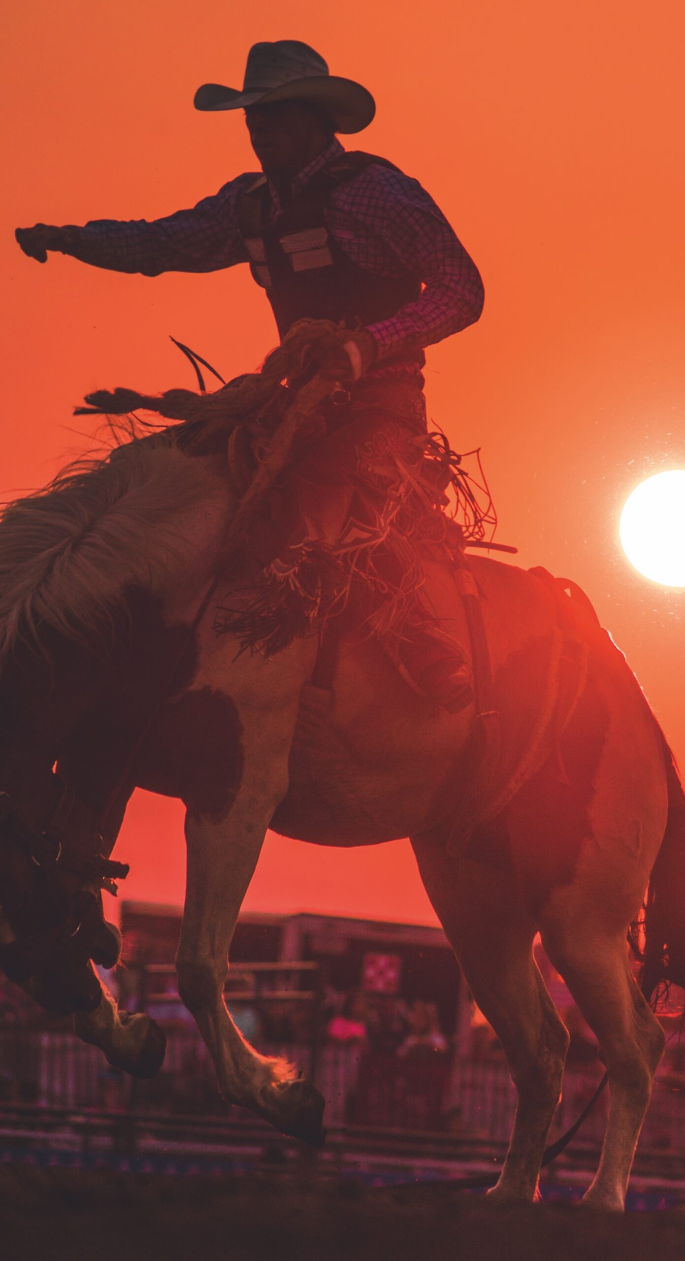 Rodeo competitor rides a bucking horse in silhouette against the setting sun. Photo courtesy of Sandhills Event Center