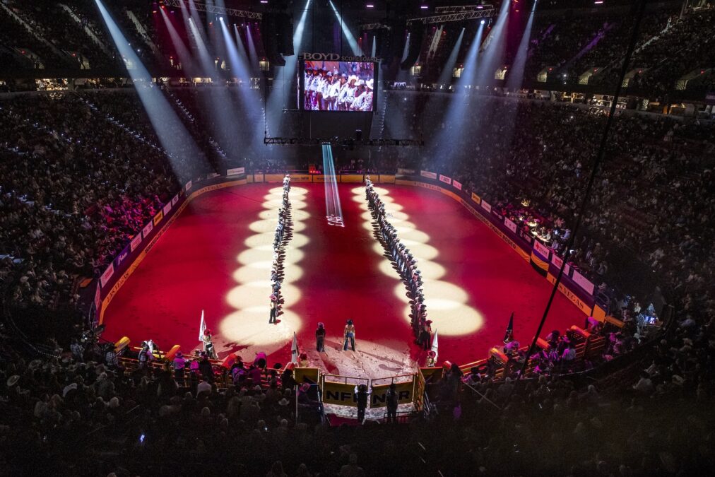 Contestants line the arena floor during the grand entry at the 2025 Wrangler National Finals Rodeo, walking into the arena rather than riding horseback. 